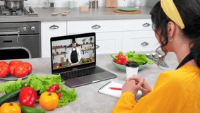 Woman in home kitchen study watch online webinar listen teacher drinking coffee tea. Man chef food blogger in laptop computer screen tells teaches student housewife shows ingredients for cooking salad