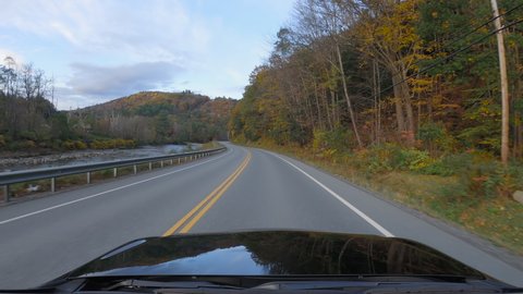 Driving a car on Vermont curvy asphalt road in Autumn. Colorful trees and mountain stream by the road side. POV