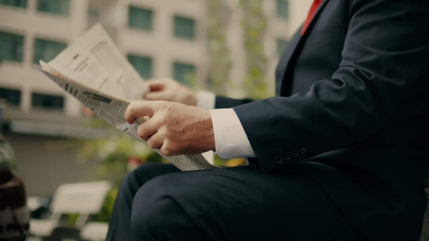 Businessman senior in an expensive suit with a beautiful beard in black blue jacket sits on bench in the park and reads a newspaper. Royalty-Free Stock Footage #1084454164