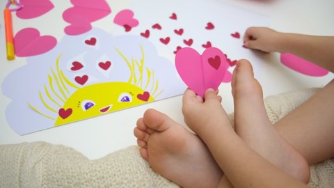 Child playing with adhesive tape paper , making funny card with sun and hearts