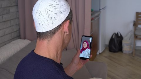 Asian muslim man makes an online video call using a smartphone and communicates with a happy smiling Muslim woman in a hijab. Lockdown, social distance during Covid-19