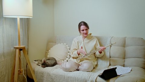 Woman musician with flute looks into tablet at home on sofa in living room