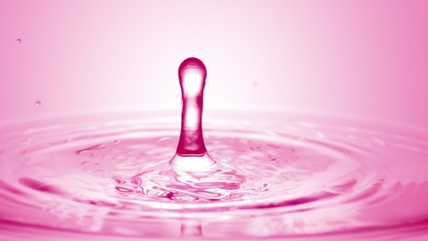 Pink drop falls down on the surface of pink transparent liquid creating concentric circles on pale pink background | Abstract skincare cosmetics formulation concept