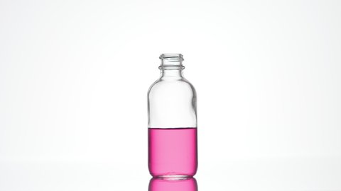 Drop of retinol is falling down into clear medical bottle with pink transparent liquid on white background | Abstract skincare cosmetics with retinol formulation concept