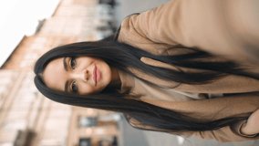 Vertical orientation portrait of cheerful brunette young woman looking at camera and talking recording vlog.  POV of cute young lady making online video call looking at camera.