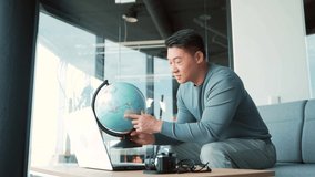 An Asian teacher conducts online distance learning using a video call webcam. E-learning is remote. School program. man teaches geography to school children with a globe in his hands