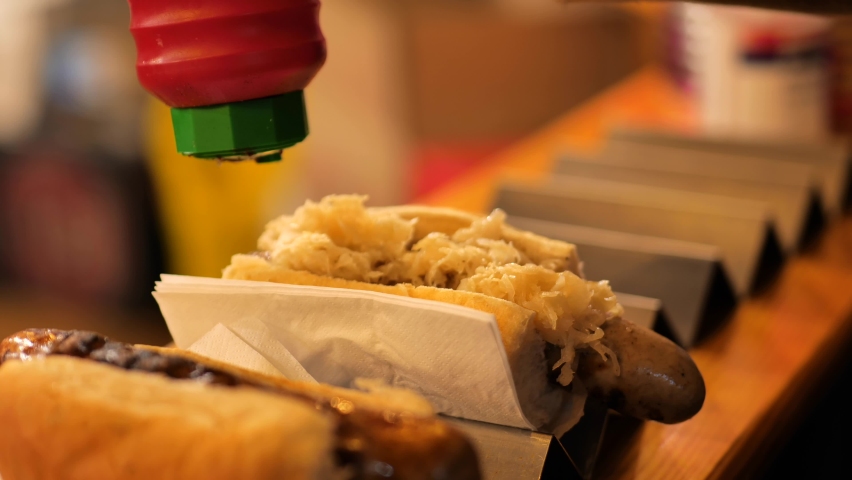 Pouring sauce from a bottle onto a sausage in a bun. Outdoor street food at a Christmas market