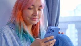 Young woman with dyed hair browsing social media news feed in cellphone. Cute girl with colored hair using mobile app on modern smartphone. 4K stock video of pretty white female with rainbow hair 