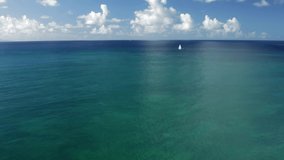 A static aerial video shot of beautiful turquoise sea water with blue sky in Caribbean island. One sailboat at distance. Pointe de Marin in Martinique
