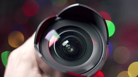 Zoom on photo video camera samyang lens. Gift ideas for a cinematographer photographer equipment. Christmas tree lights background. Hand is presenting lens flare reflections.Camera rotating.