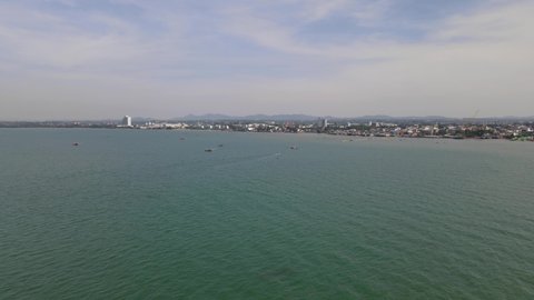 Reverse aerial footage of the sea with some fishing boats and the city of Pattaya with mountains and sky, Pattaya and Beachfronts, Chonburi, Thailand