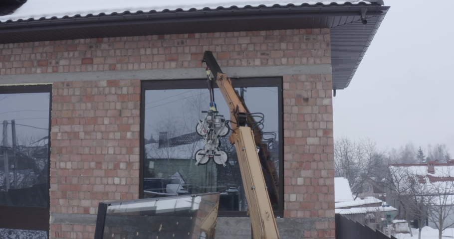 Crane installs a window with a glass vacuum lifter on the facade of a brick house in winter. General shot with drone | Shutterstock HD Video #1084488001