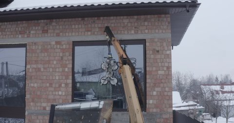 crane installs a window with a glass vacuum lifter on the facade of a brick house in winter. General shot with drone