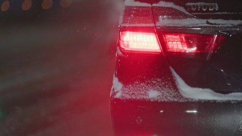 red tail light of black Toyota Camry car at night street in winter snowfall, close-up with selective focus and blurred background in Tula, Russia - December 2, 2021