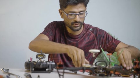 Young professional engineer examining or testing drone configuration setting using remote control while repairing drone at shop - concept of uav or quad copter repair service and hobby.