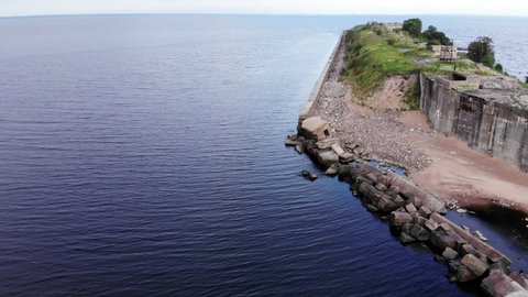 Ruined fort at Gulf of Finland, aerial shot of Obruchev at summer day. Camera fly lower, show washed out and broken concrete surrounding wall, then fly along coast of artificial island