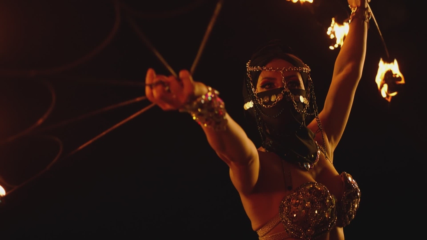 Young woman dancing performing cool and dangerous fire show and doing many tricks with fire . Dressed in black with mask closed half of face . Burning iron fire wings at night. Asian , Arabian culture