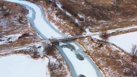 4K High aerial of an old iron bridge spanning a frozen, snow covered river during winter in the midwest