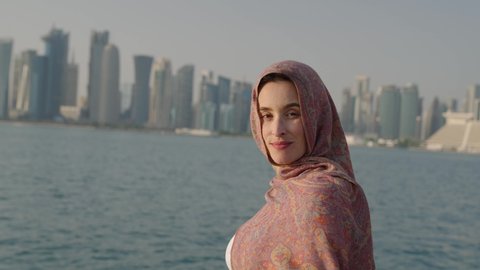 Portrait of beautiful young Arab muslim woman on a dhow boat ride looking straight to camera and smiling. Doha Skyline behind in slow motion
