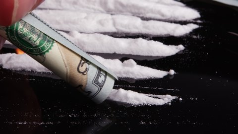 4k shot of Cocaine snorted on a black glass through rolled 100 dollar bank note, close up view. Good for use as part or background in Healthy (unhealthy) Life, Medical, Anti Narcotism, Crime concepts