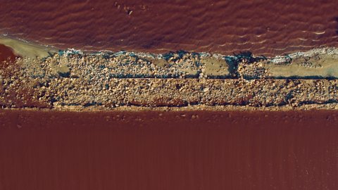 Top view pink sea water surface. Aerial salt lake red water surface. Unusual water color with minerals. Colourful pink water splashing sand beach. Drone view romantic seacoast with red sea surface.