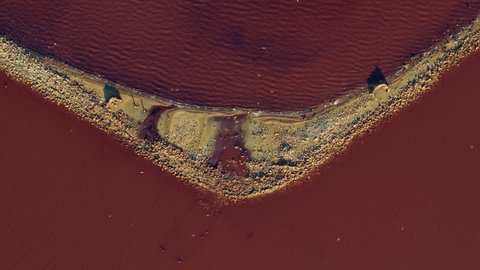 Pink sea waves splashing sandy beach at red water surface at summer. Top view salt mineral island at pink lake. Aerial view unusual island with small birds at pink water. Tranquil meditative seascape