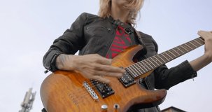 rock blonde girl, close up playing an electric guitar on the roof of an old building, front view. Musical video clip shooting. Outdoor show.