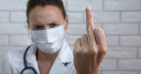 Doctor fuck gesture. A view of a doctor in protective mask with a fuck gesture to her work.