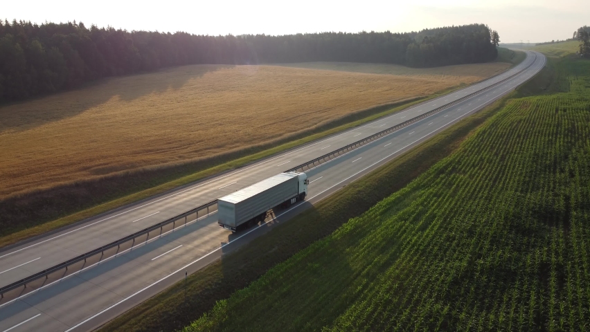 Heavy truck is carrying cargo on the highway in a beautiful area at dawn. Lorry rides through the countryside with beautiful landscape at background. International Trade, Cargo Delivery, Cargo	
