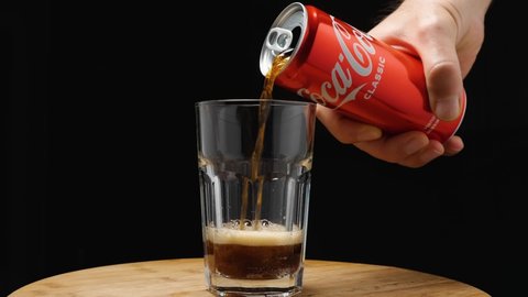 A man's hand holds a red can of Coca-Cola and pours it into a highball glass. The camera flies around. Parallax effect. Slow motion. Russia, Krasnodar, December 24, 2021