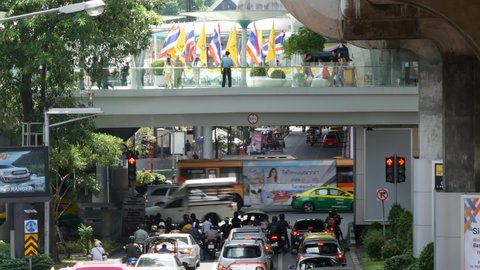 BANGKOK, THAILAND - 11 JULY, 2019: Intersection on busy city street. People on motorcycles and cars riding on crossroad under pedestrian bridge on busy street