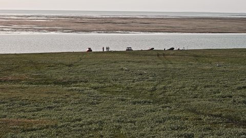Faraway view of people silhouettes standing and walking near boats that are near the river on shore. Research in Yamal Peninsula.