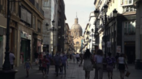 Blurred defocused view of people wear face masks as precautionary measures during coronavirus. Street with the Cathedral Basilica of Zaragoza city. A Roman Catholic church of Spain.