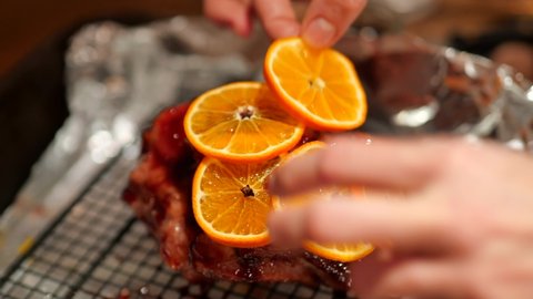 Dressing a Christmas Ham with orange slices and cloves before roasting in an oven