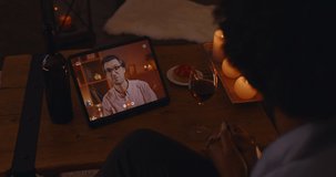 Happy mixed race couple having online dating on tablet while staying at home. African woman and caucasian man sending air kisses to each other. Romantic atmosphere during evening time.