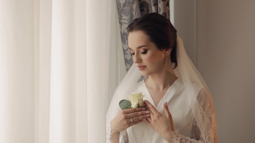 Lovely bride in wedding luxury boudoir dress, night gown with wedding bouquet for groom in the hands. Pretty and well-groomed woman. Wedding preparation, happy moments, morning. Indoors, slow motion