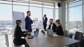 Colleagues sitting at the table in front of laptops and listening to the speaker. Male partner standing at the window and speaking on the phone at the backdrop. - Powered by Shutterstock - Get 15% off with code: PIKWIZARD15