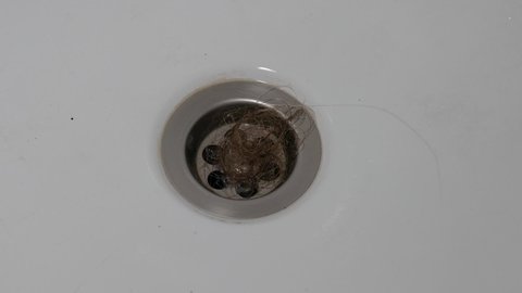 A bundle of loose women's hair in a sink drain. Close-up. The problem of early hair loss