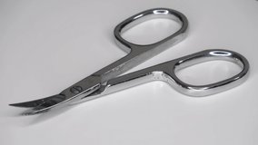 Loopable selective focus of small metal scissors spinning on white background.