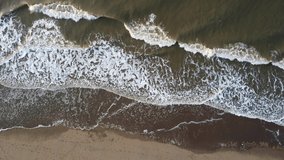 Top down view on rough sea waves. The waves sway on the beach due to local currents and winds while a man enjoys nature. Useful as summer and travel vacation concept, 4k aerial perspective.