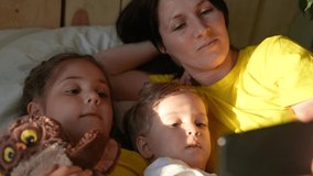 happy family at home. mom baby son and daughter watching online video on a fun smartphone gadget lying in bed at home. sunlight from window morning. happy family online video chat mom and baby kids