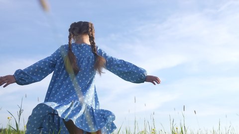 child girl a dancing in the field park. happy childhood family friendship concept. girl kid whirls in a blue dress in grass in the summer park. daughter in dancing whirls in the summer in sun nature