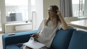 A young woman sitting on a sofa with a TV remote control in her hands and switching channels - Powered by Shutterstock - Get 15% off with code: PIKWIZARD15