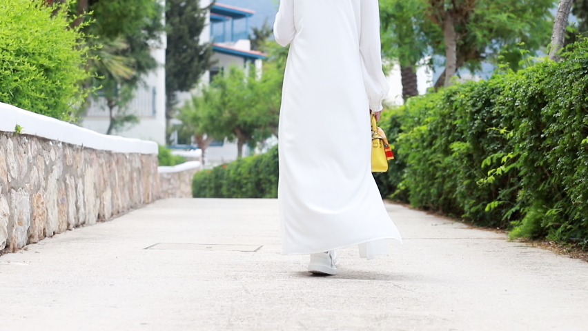 Cinematic slow motion Young woman in white dress walks holding a hat walking through the streets of greece