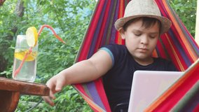 boy resting in a hammock in nature with a laptop. drinking a cocktail. communicates with friends online, conducts a stream, sends a blog. modern youth, teenager. Plays a video game. Blogger.