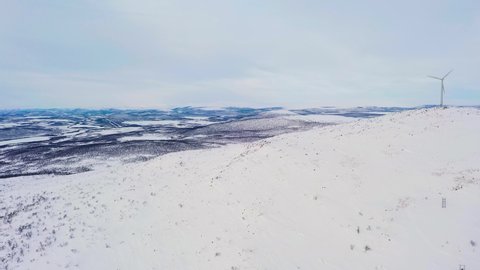 Aerial view of a mountain and arctic wilderness with windmills, winter in Enontekio, Finland - reverse, tilt, drone shot