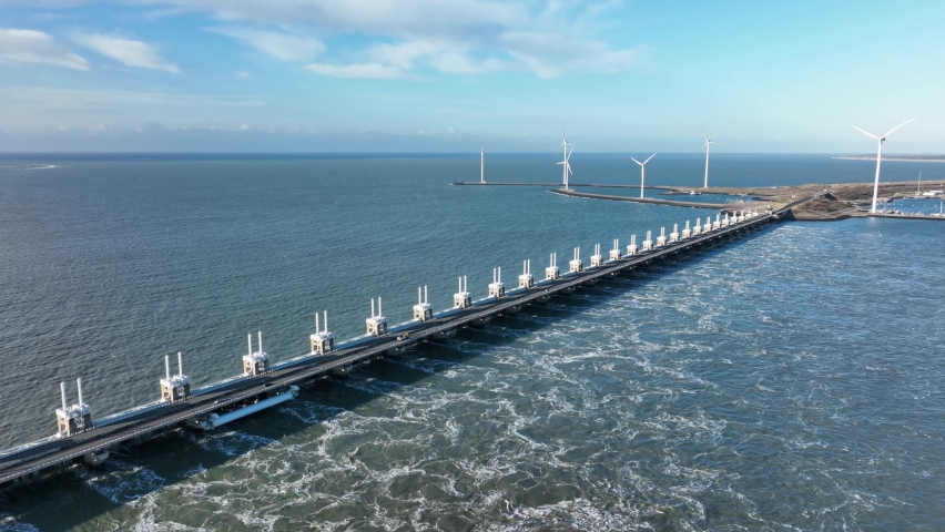 High aerial shot of water flowing through the opened sluices of the Eastern Scheldt storm surge barrier in Zeeland, the Netherlands, on a beautiful sunny day | Shutterstock HD Video #1084540948