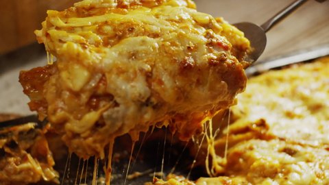 Isolated portion of delicious lasagne with greasy melted cheese dripping, dish