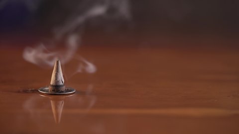 Incense cone sitting on a warming brown surface burning and smoking.
