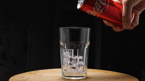 A man's hand from a can pours Coca-Cola into a glass with ice. The camera flies around. Parallax effect. Dark background. Russia, Krasnodar, December 24, 2021